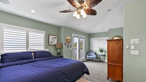 A bedroom with a large bed, a ceiling fan, a wooden cabinet, and a small table with a plant. - Coastal Haven w/ Large Rooftop Deck & Beach Access 🏖️ (Oceano)