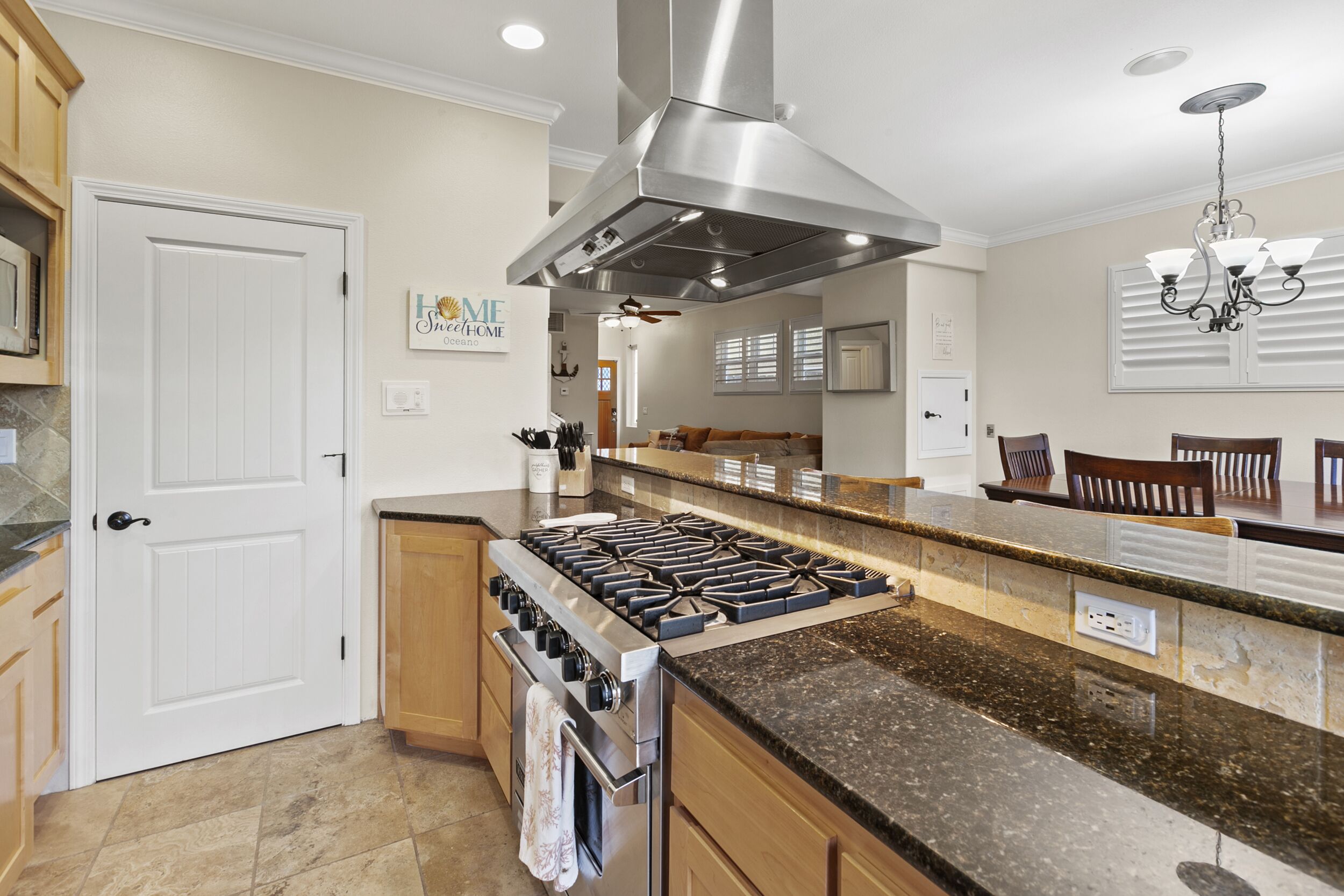 A kitchen with a central island, stainless steel range hood, wooden cabinets, and a dining area with chairs.