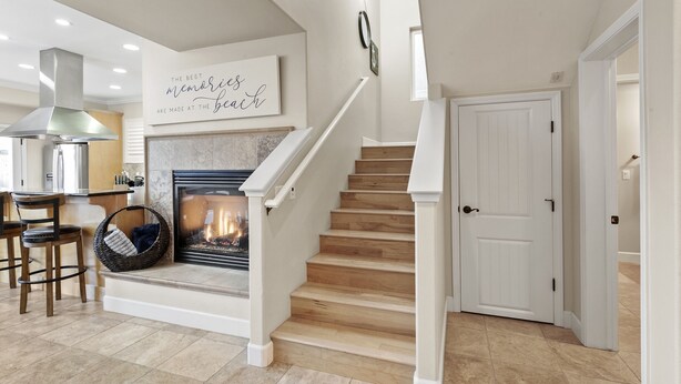 A staircase leading to a door, a fireplace with a fire, and a kitchen area with a dining table and chairs. - Coastal Haven w/ Large Rooftop Deck & Beach Access 🏖️ (Oceano)