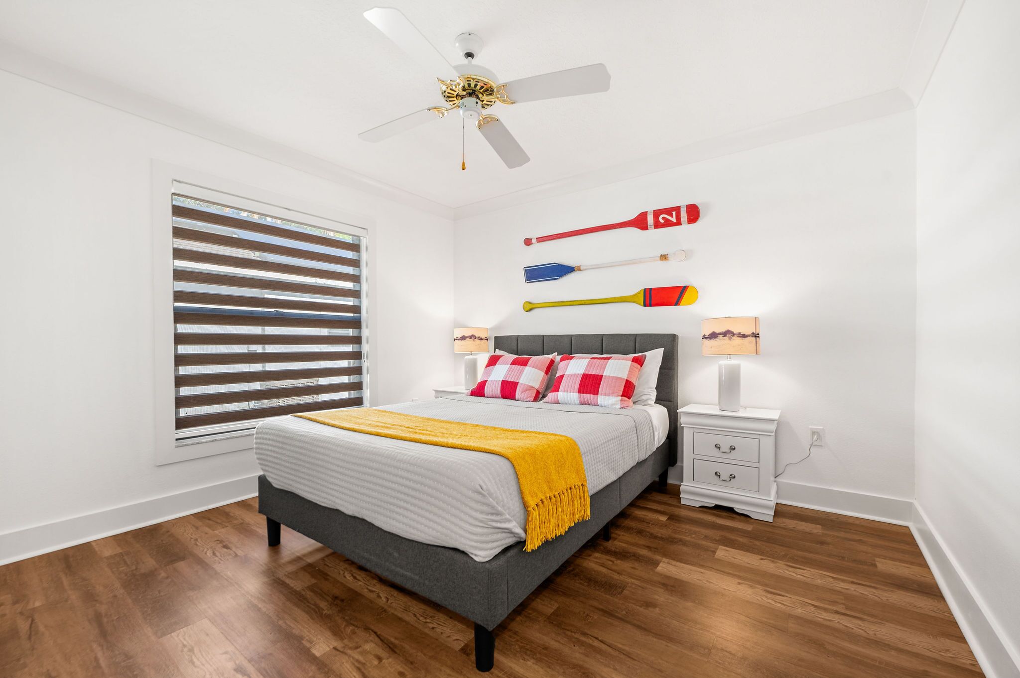 A bedroom with a bed, nightstands, a ceiling fan, and a window with blinds.