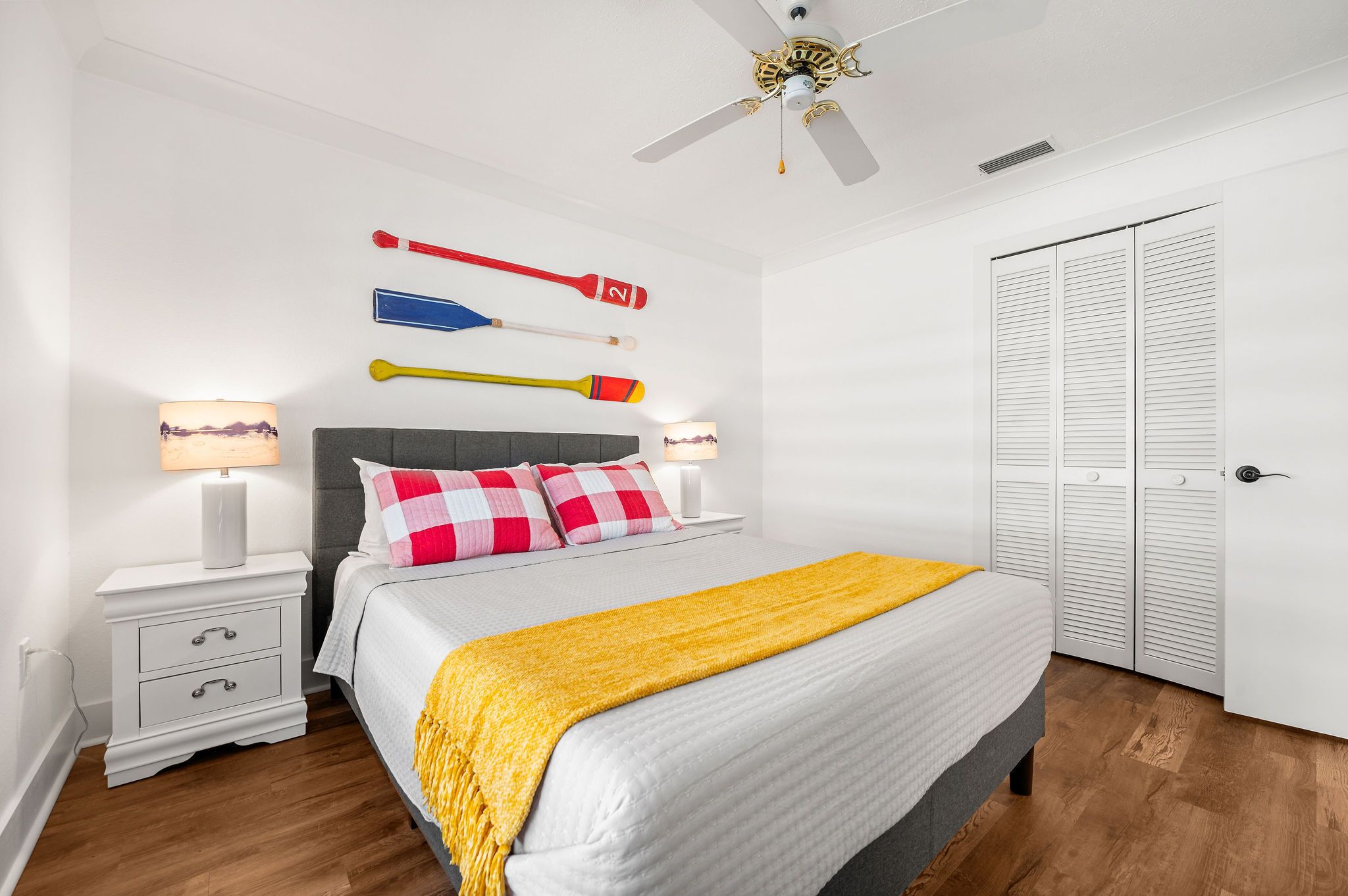 Quarto bem organizado com cama, mesas de cabeceira, um guarda-roupa e ventoinha no teto.