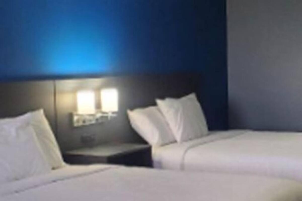 Habitación de hotel con dos camas, una mesita de noche y un baño visible a través de una puerta abierta.