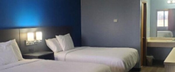A hotel room with two beds, a nightstand, and a bathroom visible through an open door.