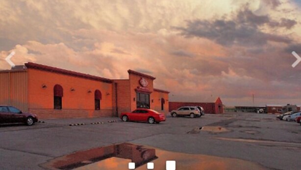 A parking lot with a building that has a clock tower and arched windows.