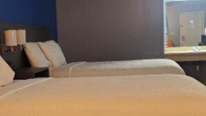 A hotel room with two beds, a nightstand, and a lamp.