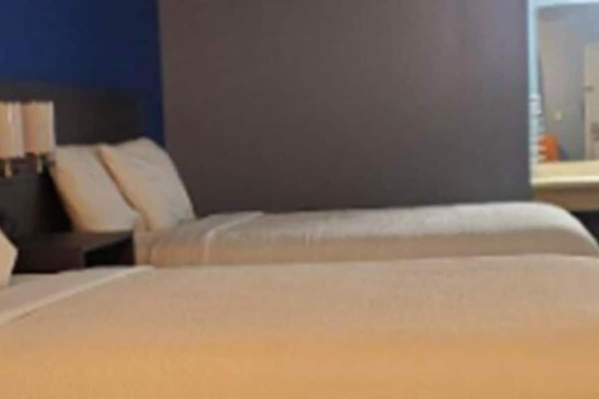 Habitación de hotel con dos camas, una mesita de noche y una lámpara.