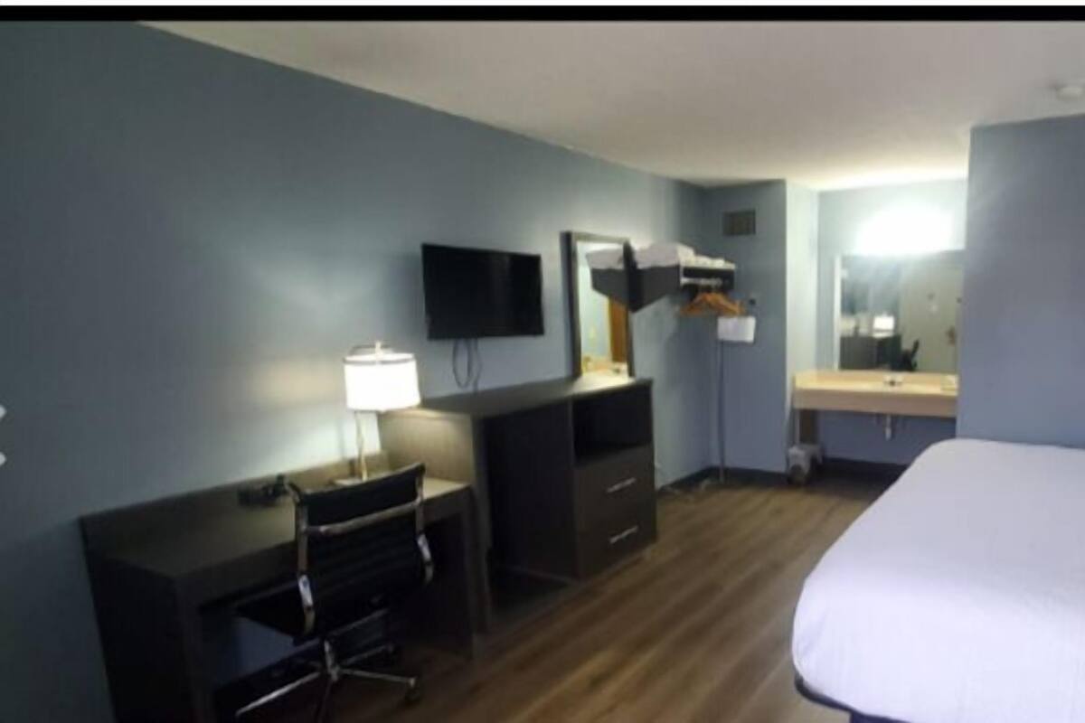 Una habitación de hotel con cama, escritorio, silla, televisor y espejo.