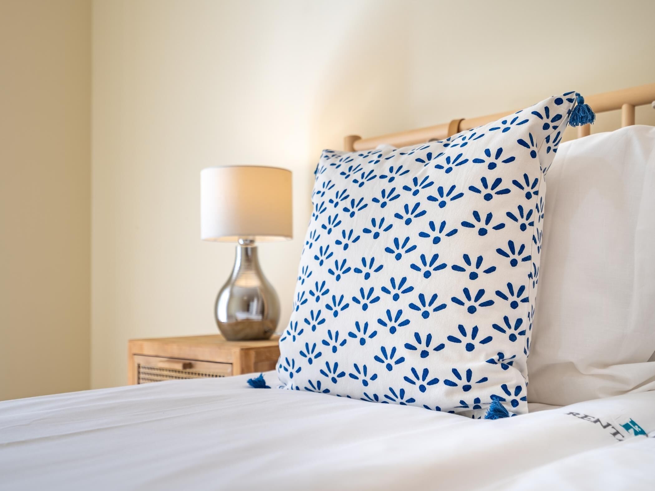 A neatly made bed with white bedding and a blue floral pillow.