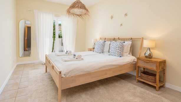 A bedroom with a wooden bed, white bedding, a bedside lamp, a mirror, and a view of the outdoors. - Cozy Retreat for Couples in Burgau (Burgau)