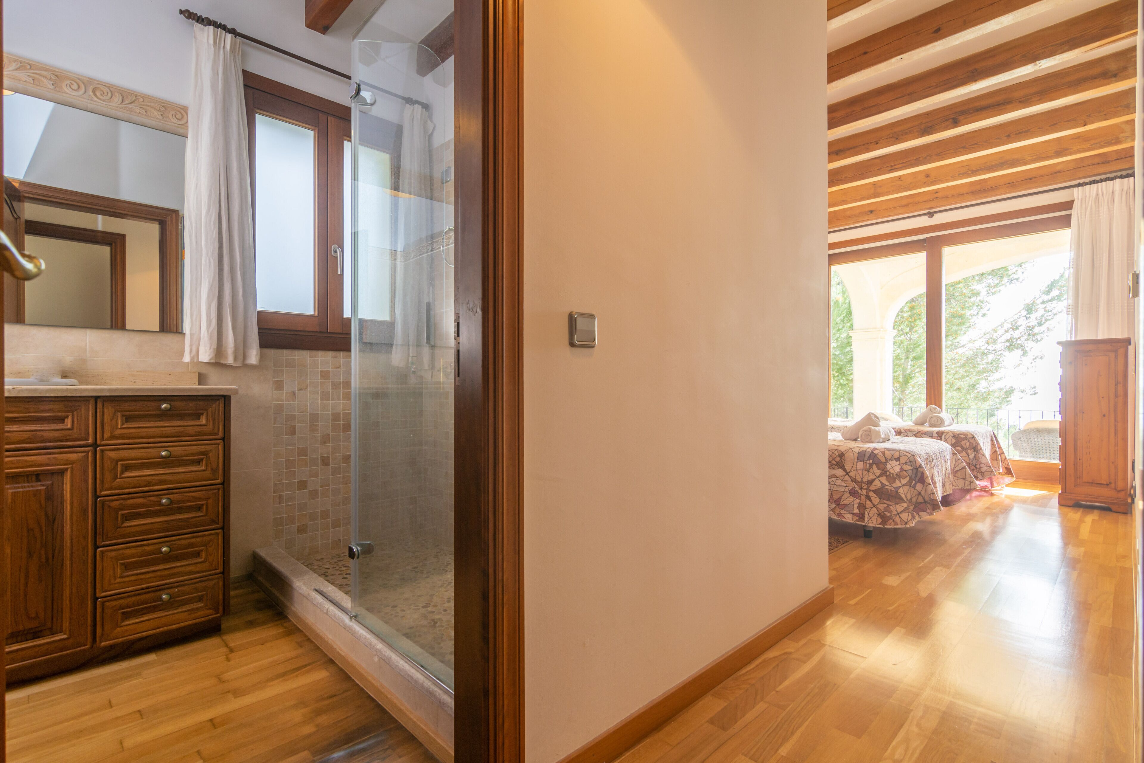 Una habitación de hotel con piso de madera, cabina de ducha de vidrio, armario de madera y una cama con colcha estampada.