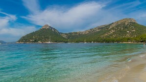 Une plage avec une eau turquoise et limpide, un rivage sablonneux et une montagne en arrière-plan.