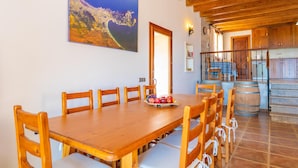 Un coin repas avec une table et des chaises en bois, un tableau au mur et un espace cuisine doté de meubles en bois et d’un escalier.