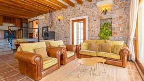 Un salon avec des canapés en cuir, un mur en pierre, des poutres en bois, une cheminée et un escalier.