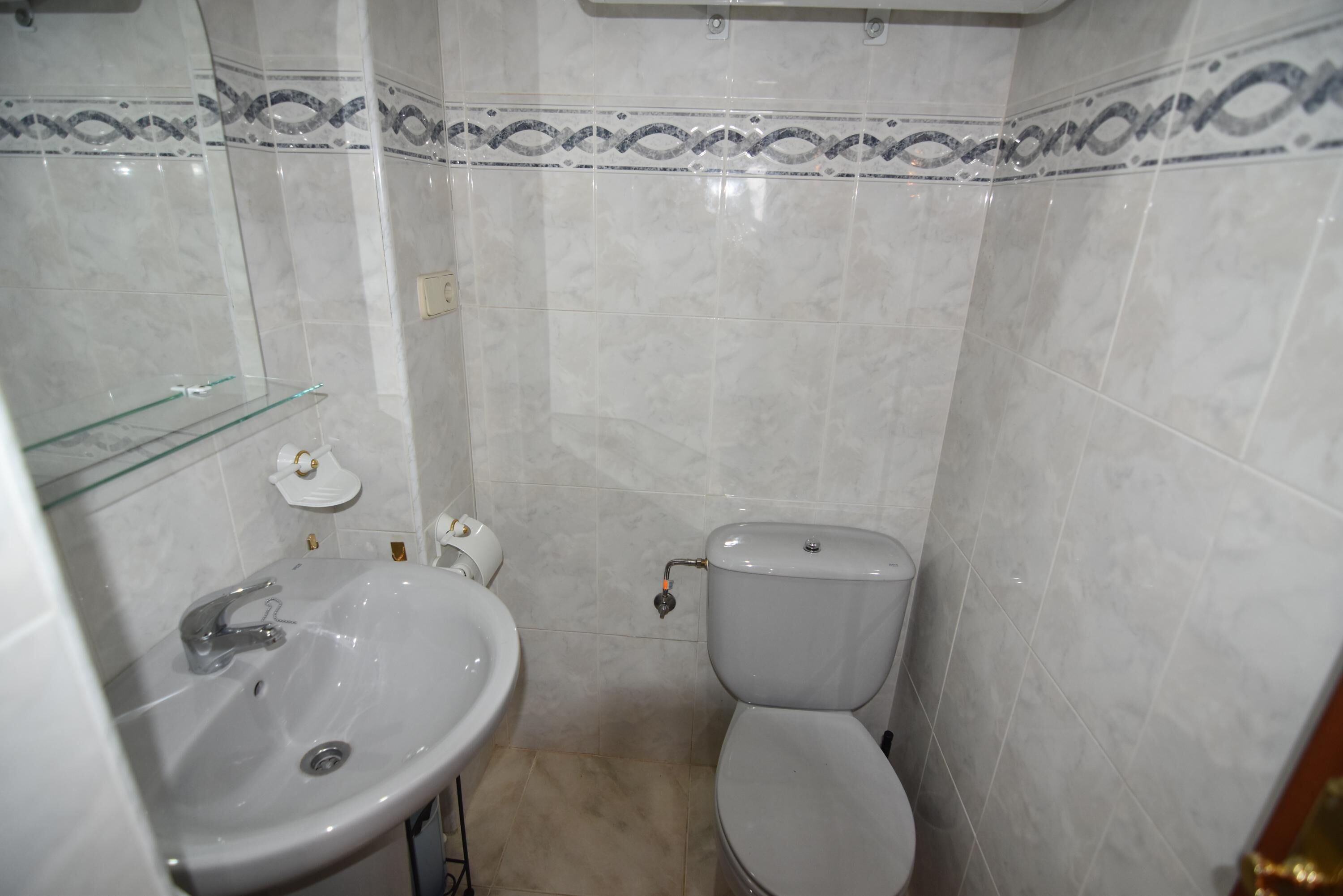 A bathroom with a white sink, toilet, and glass shelf.