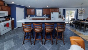 A modern kitchen with a central island, bar stools, and a dining area with a chandelier. - Private, Updated Baileys Harbor Home: The Roost (Baileys Harbor)