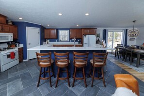 Een moderne keuken met een centraal eiland, barkrukken en een eetgedeelte met een kroonluchter.
