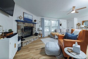 Een woonkamer met een open haard, een bank, een salontafel en een plafondventilator.