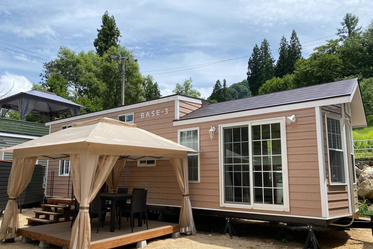 Una casa móvil con terraza y zona de estar al aire libre, identificada como BASE-3.