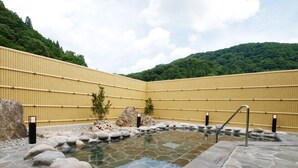 Un onsen japonés tradicional con piscina de piedra, pared de bambú y paisaje rocoso.