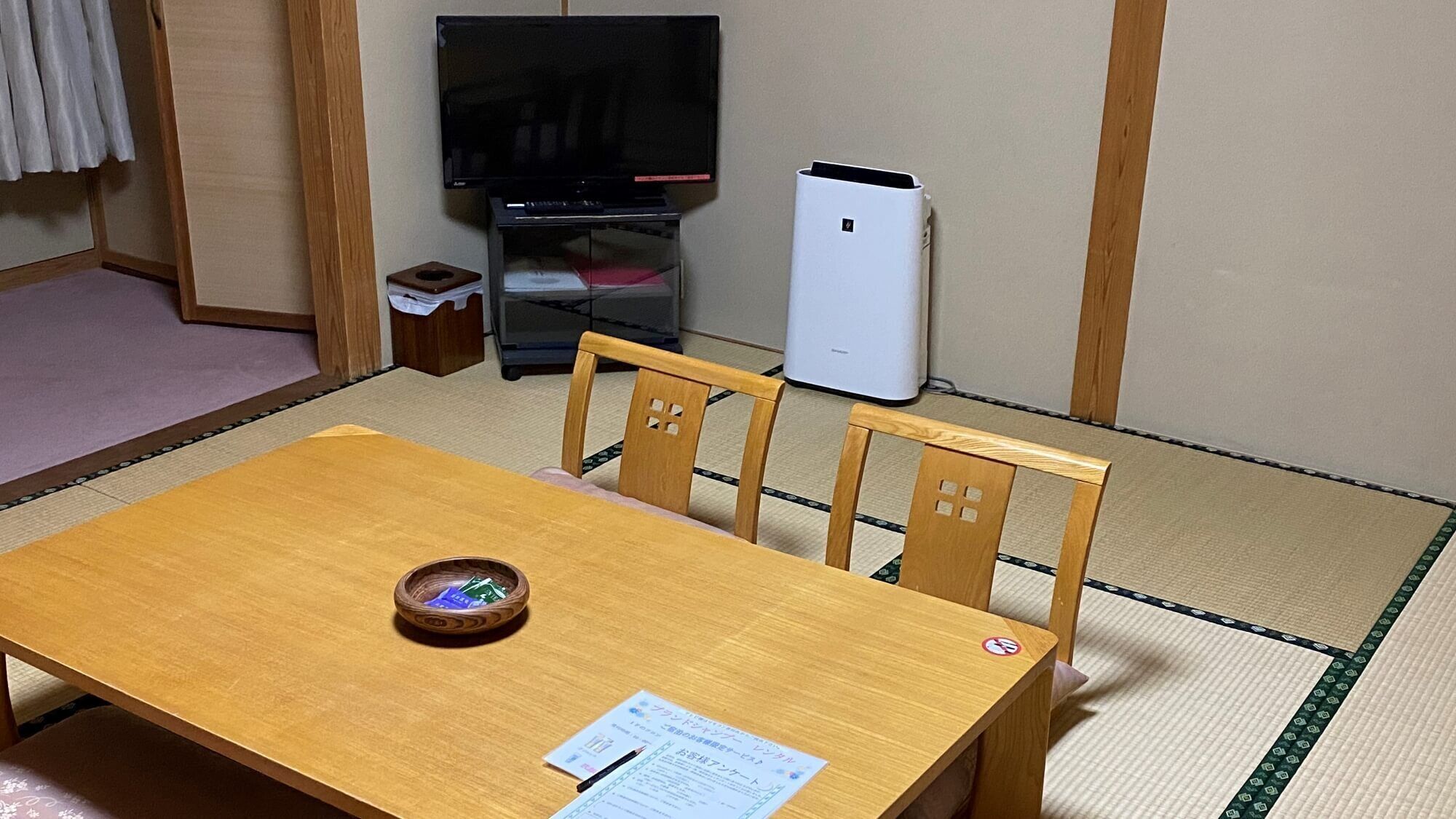 A room with tatami flooring, a wooden table with a bowl, a television, and a white appliance.