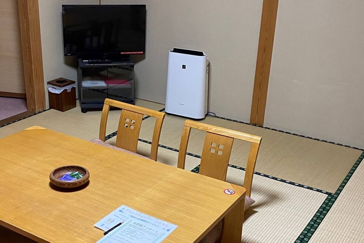 Una habitación con suelo de tatami, una mesa de madera con un cuenco, un televisor y un electrodoméstico blanco.