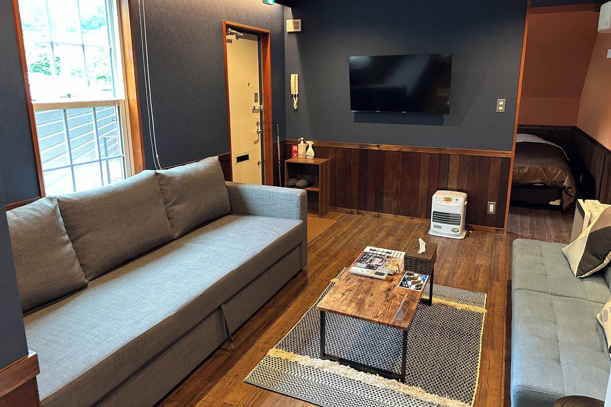Un espacio habitable compacto con sofá, mesa de centro, televisión y una cama pequeña.