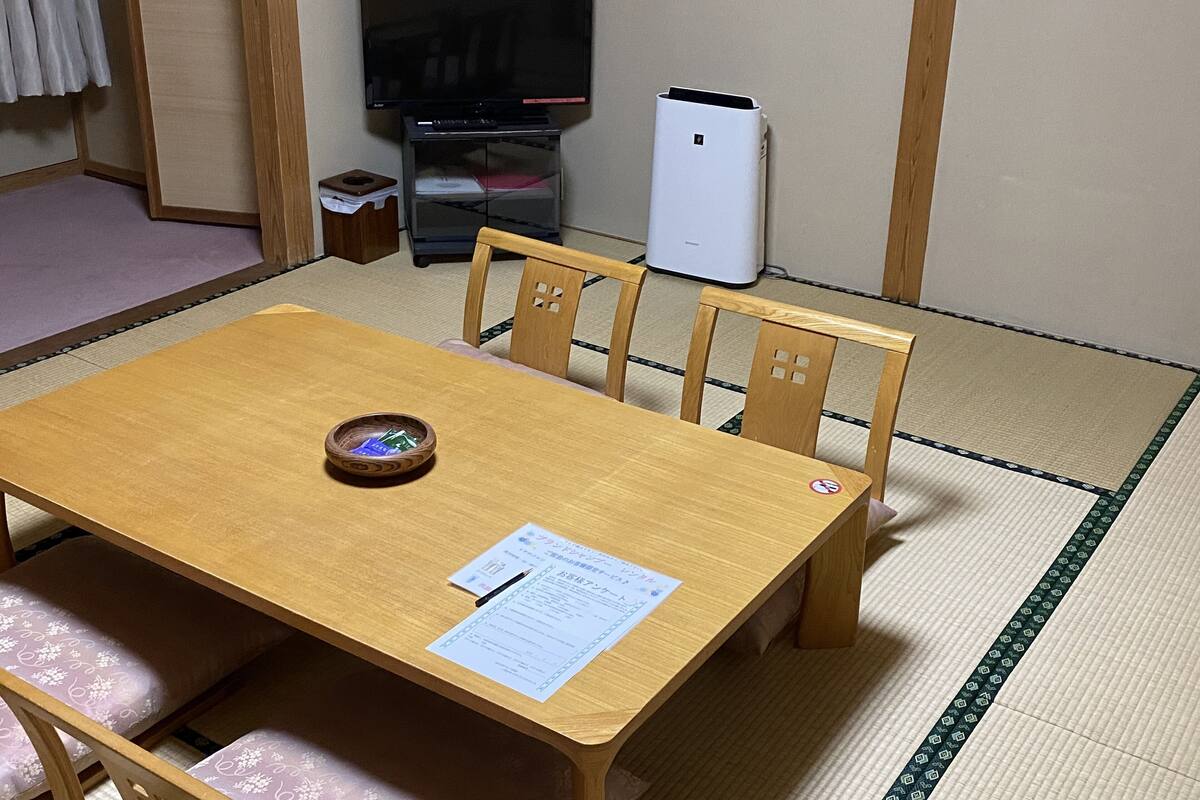 Una habitación tradicional japonesa con suelo de tatami, una mesa de madera con un cuenco, un televisor y un refrigerador.