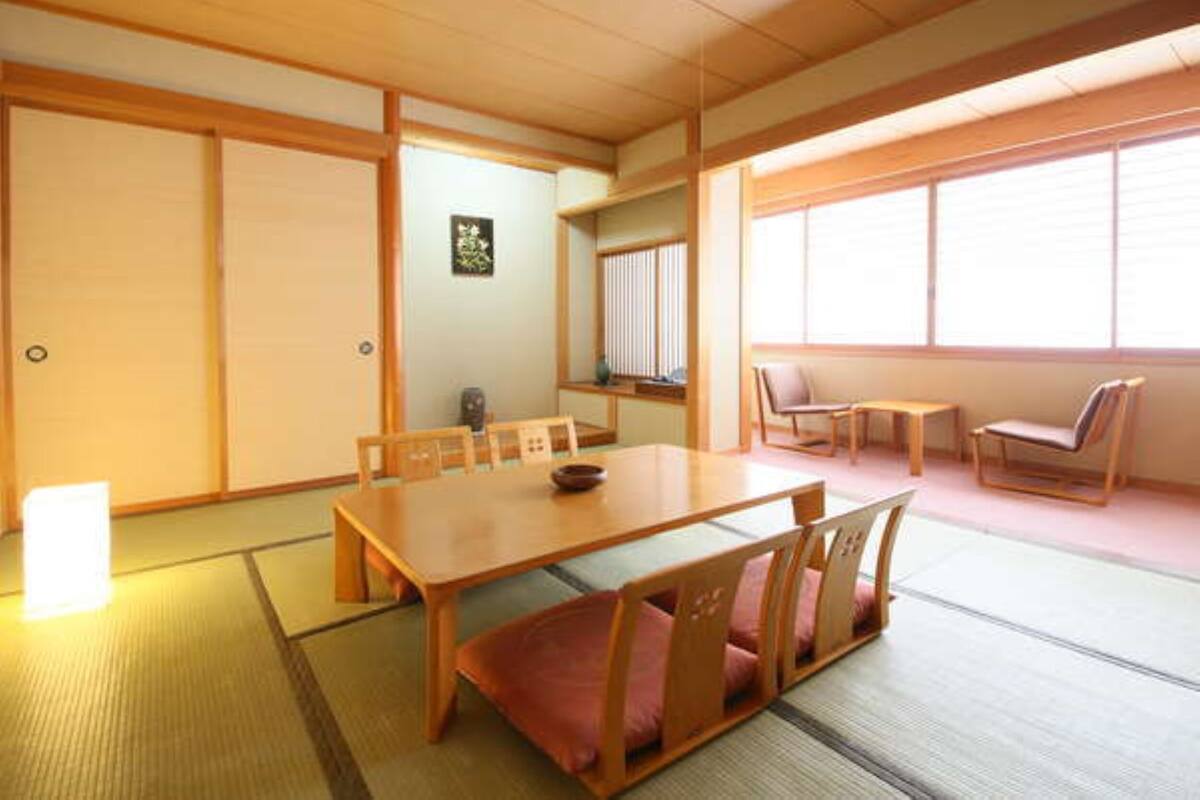 Una habitación japonesa tradicional con suelo de tatami, una mesa de madera para comer con cojines y puertas correderas.