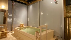 Una terraza de madera con un jacuzzi, un taburete de madera y una barandilla de vidrio.