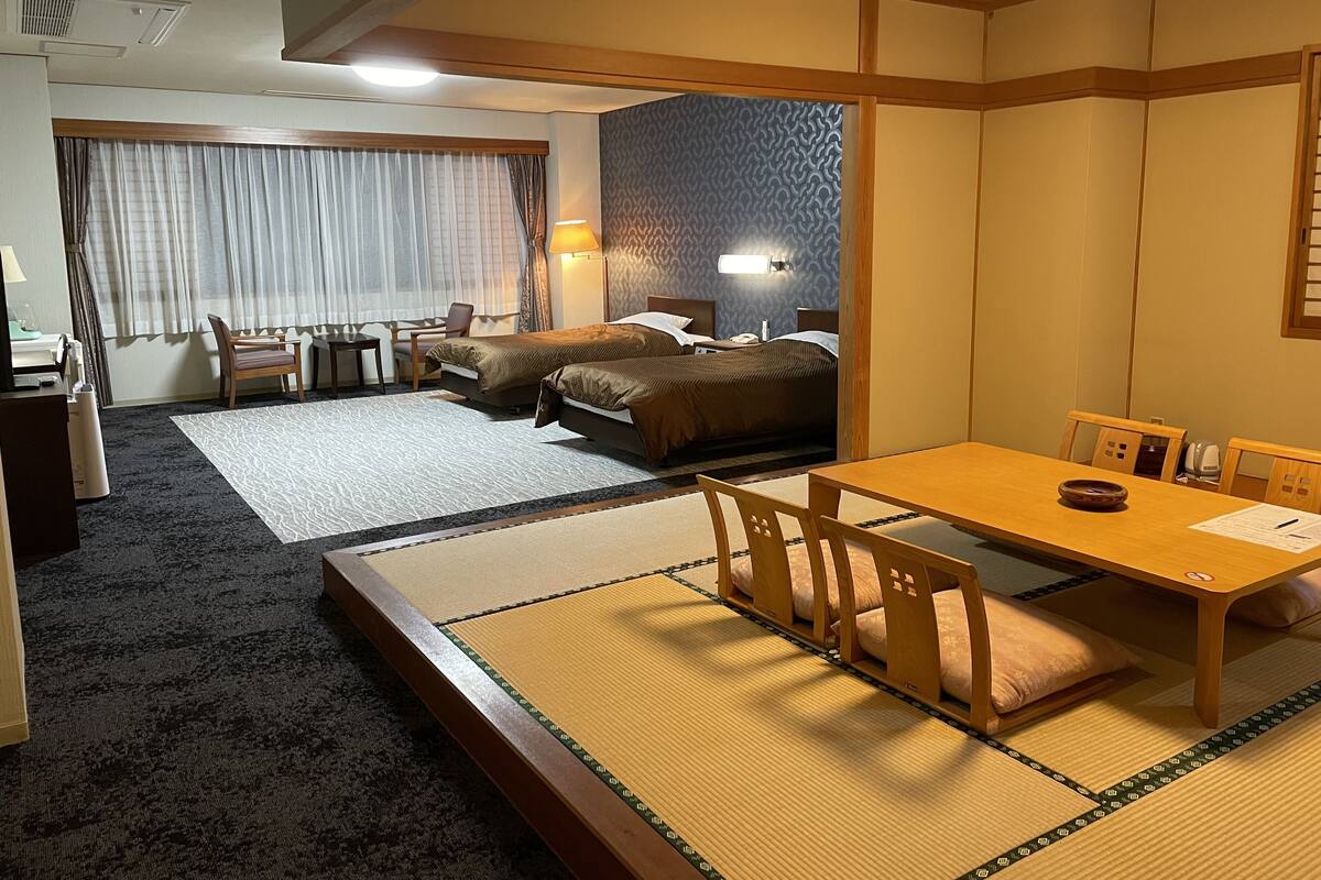 Una habitación tradicional japonesa con esteras de tatami, una mesa baja con un cuenco y una cama con un muro estampado de fondo.
