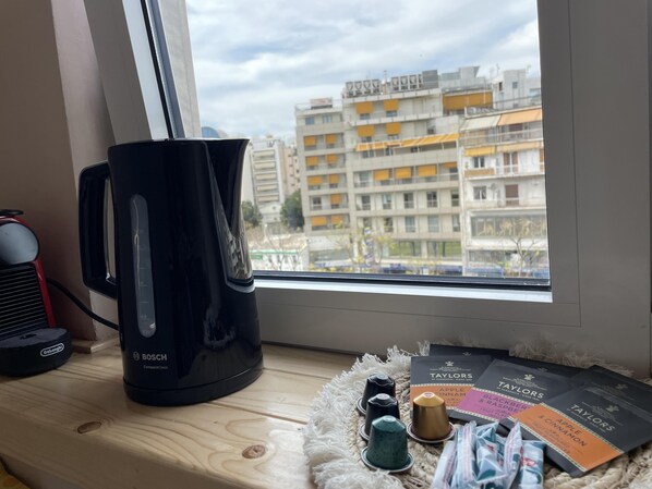 A room with a window overlooking a cityscape, a black BOSCH compact coffee maker, and a tray with tea bags and a book.