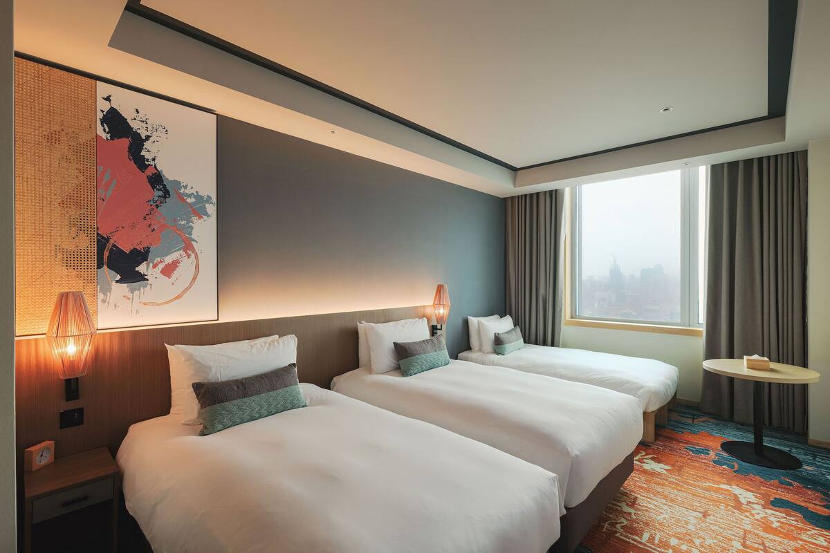 Een hotelkamer met twee bedden, een groot raam, stadszicht en een modern interieur.