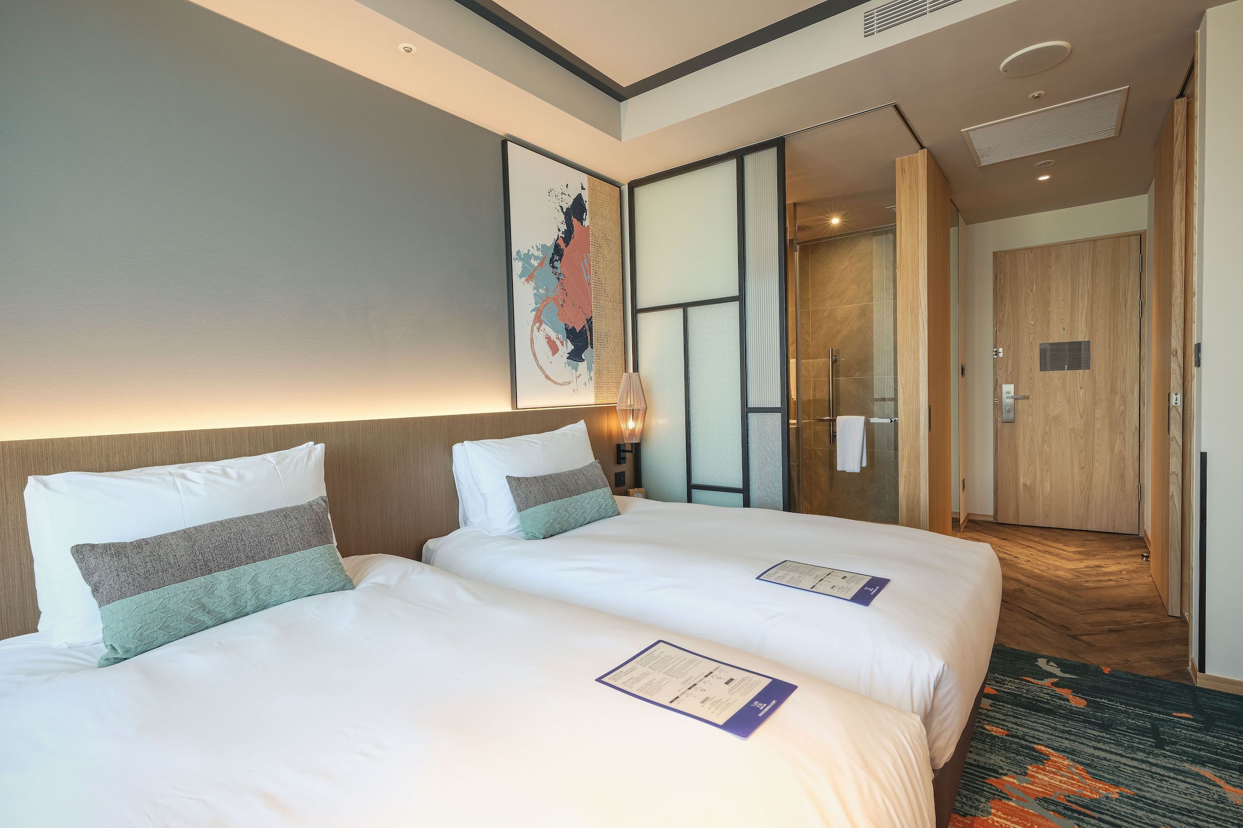 A hotel room with two beds, a large abstract painting, a wooden door, and a carpeted floor.
