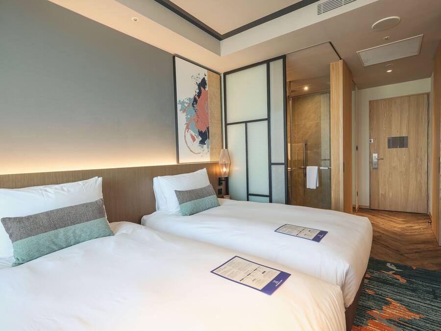 A hotel room with two beds, a large abstract painting, a wooden door, and a carpeted floor.