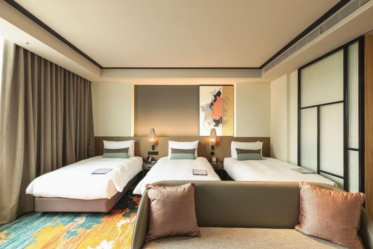 A hotel room with two beds, a sofa, a large window, and a painting on the wall.