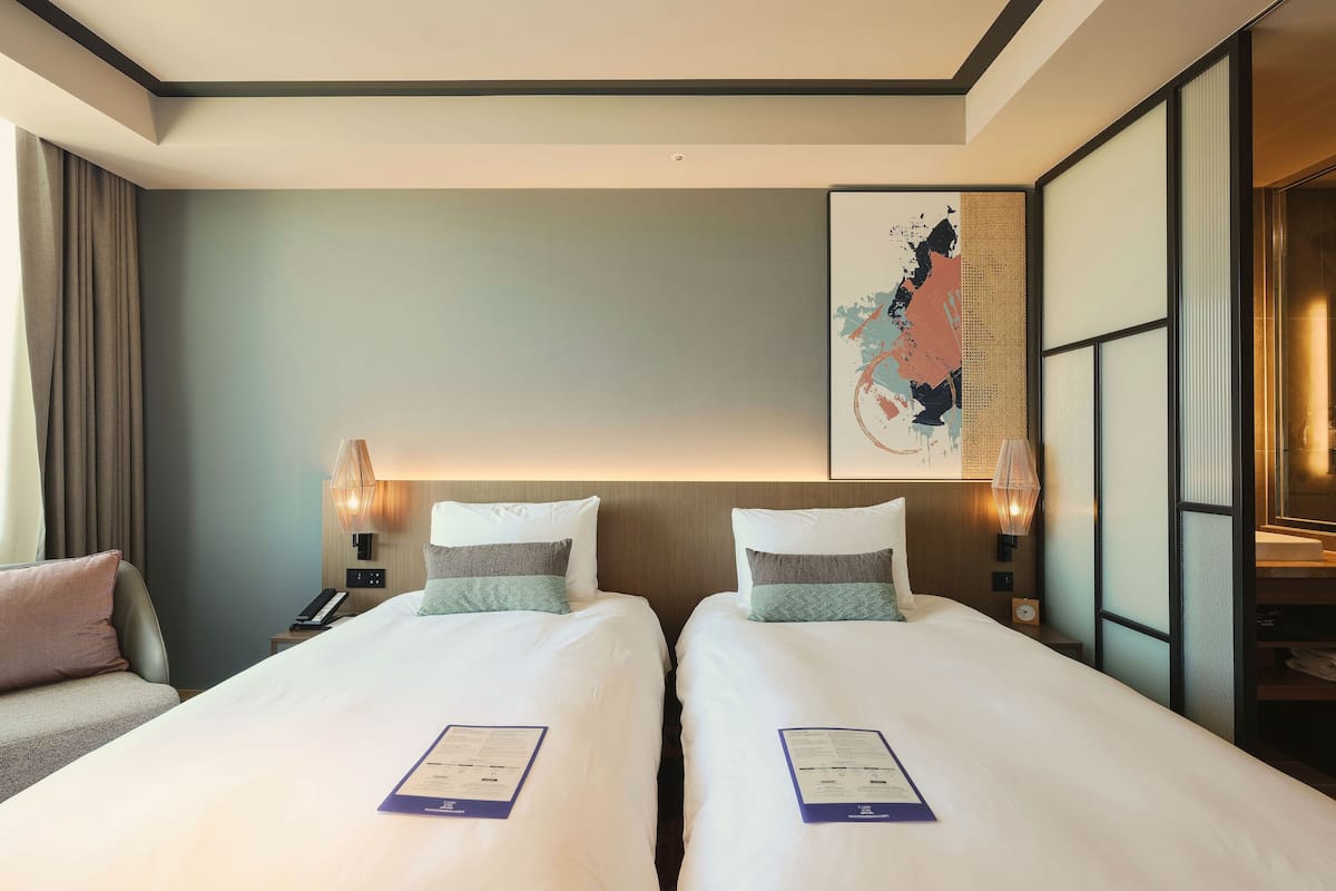 Une chambre d’hôtel avec deux lits, une table de chevet avec un téléphone, une lampe et un tableau décoratif au mur.