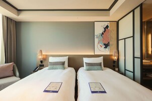 A hotel room with two beds, a nightstand with a phone, a lamp, and a wall art piece.
