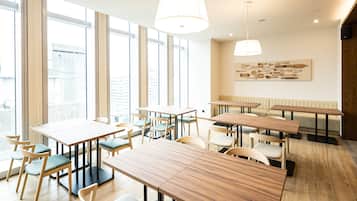 Un comedor moderno con mesas y sillas de madera, ventanas amplias e iluminación colgante.