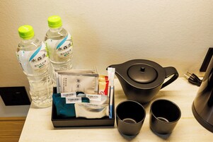 Disposição de café da manhã em quarto de hotel, com duas garrafas de água, um conjunto de chá, uma bandeja com amenities e duas xícaras pretas.