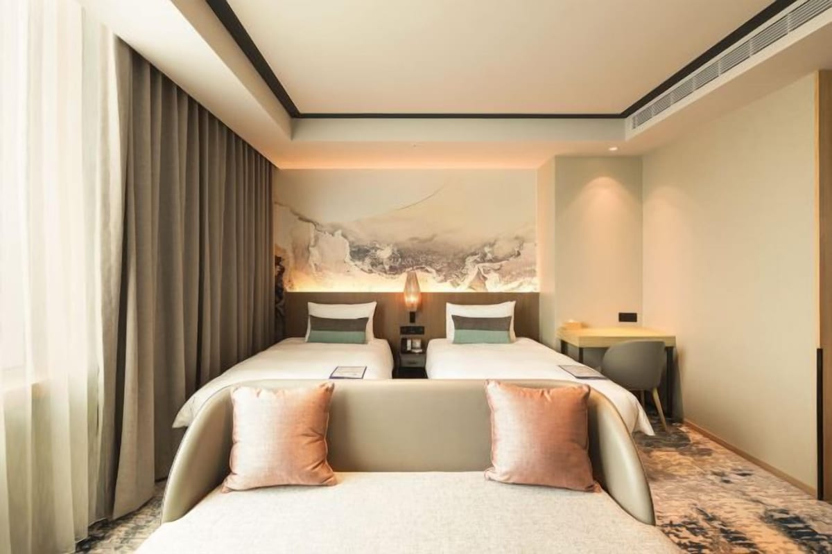 A hotel room with two beds, a desk, and a large abstract painting on the wall.