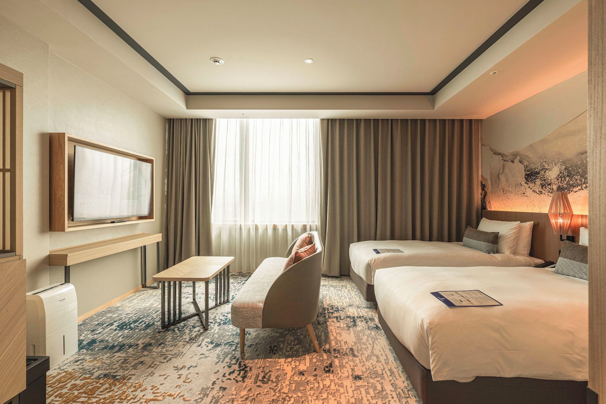 A hotel room with a bed, a desk, a chair, a TV, and a large window with curtains.