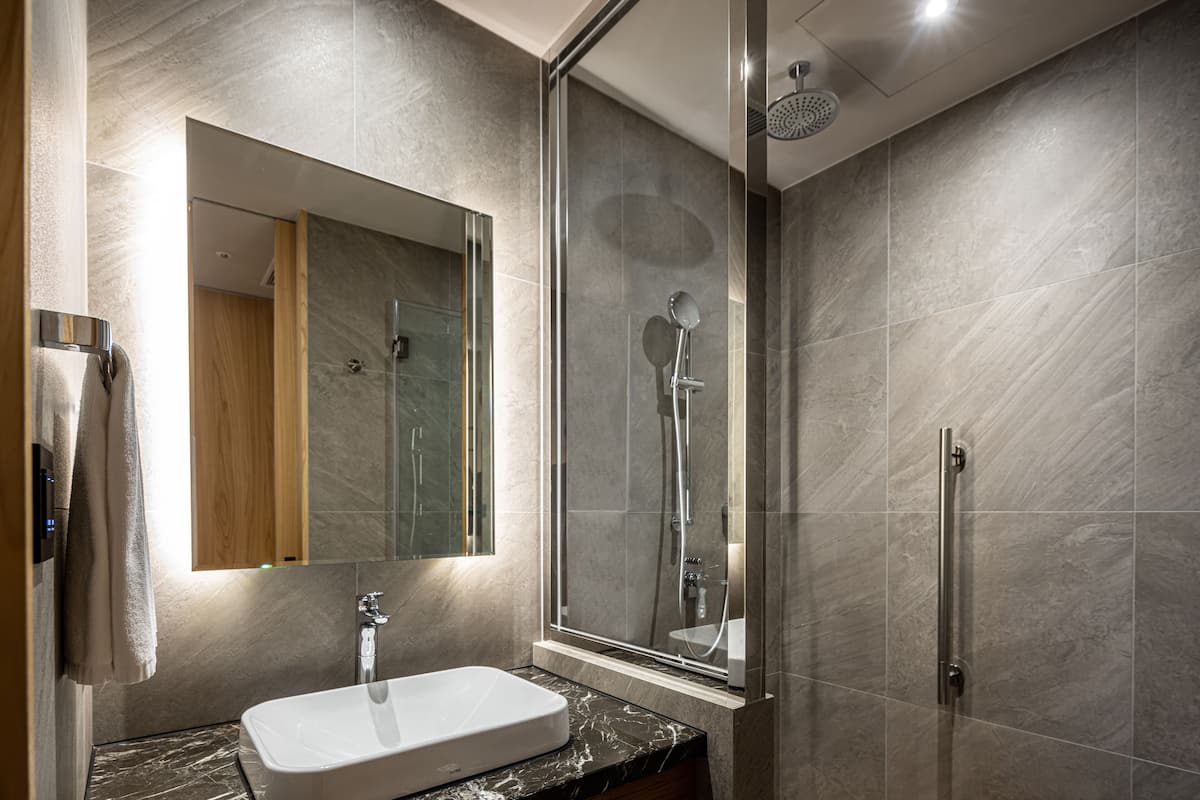 Une salle de bain moderne dotée d’une douche à parois de verre, d’un grand miroir et d’un comptoir en marbre.