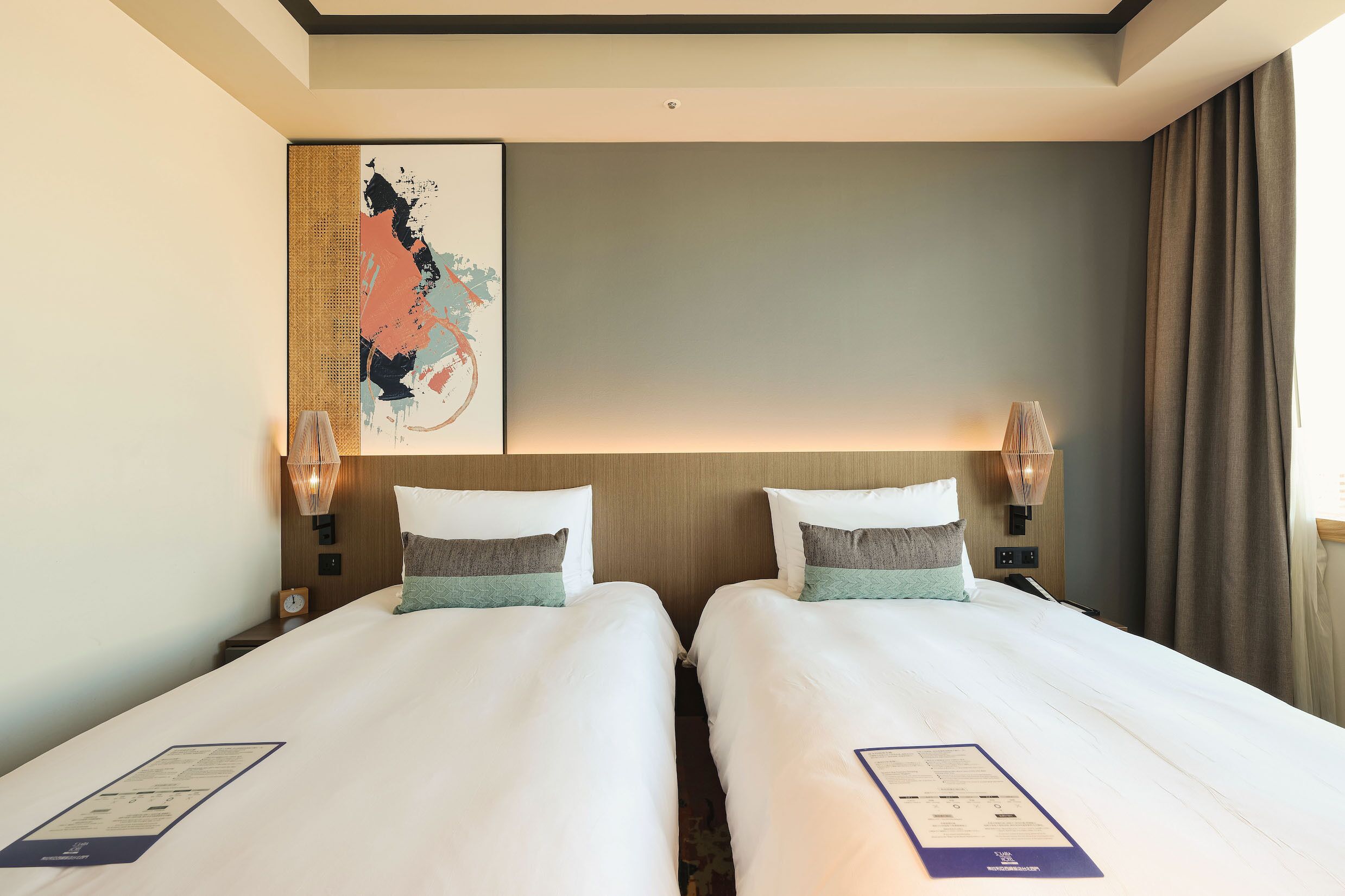 Een hotelkamer met twee bedden, een groot abstract schilderij en een nachtkastje met een lamp.