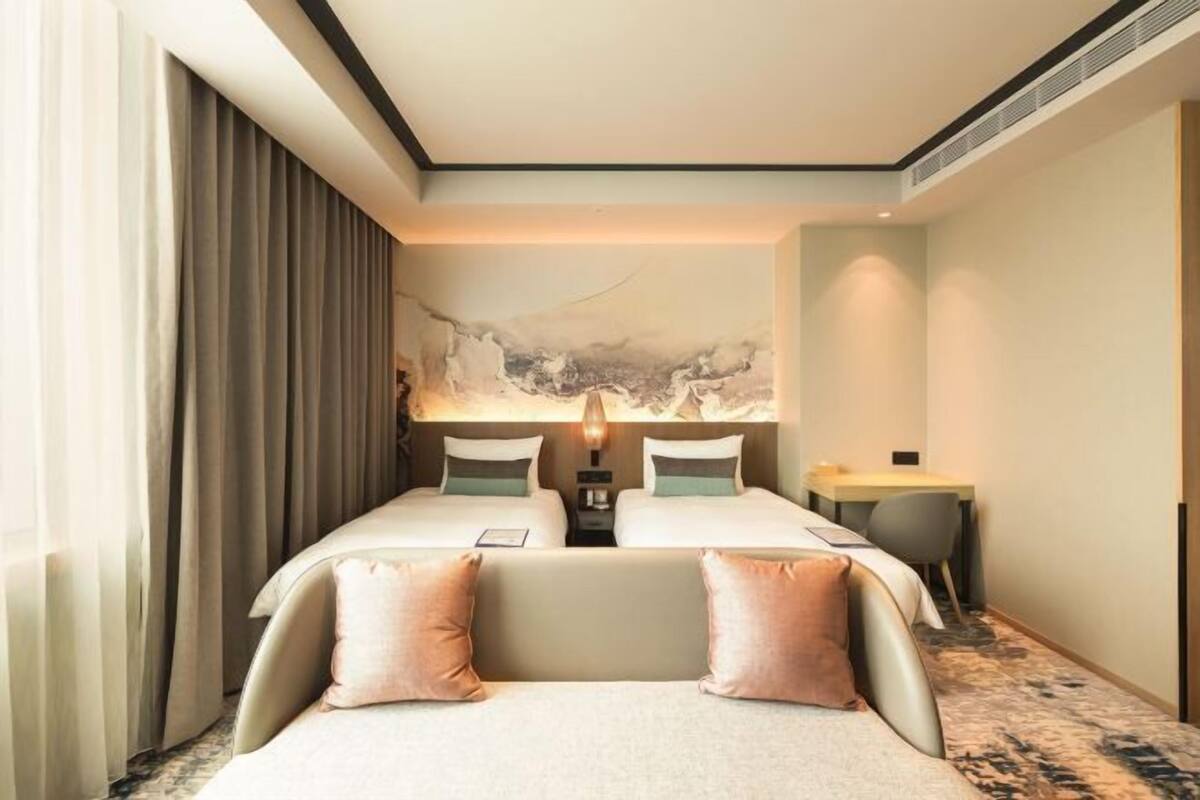 Een hotelkamer met twee bedden, een bureau en een groot abstract schilderij aan de muur.