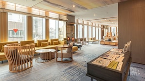 A spacious lobby with a modern design, featuring a mix of seating areas, a coffee bar, and a reception desk.