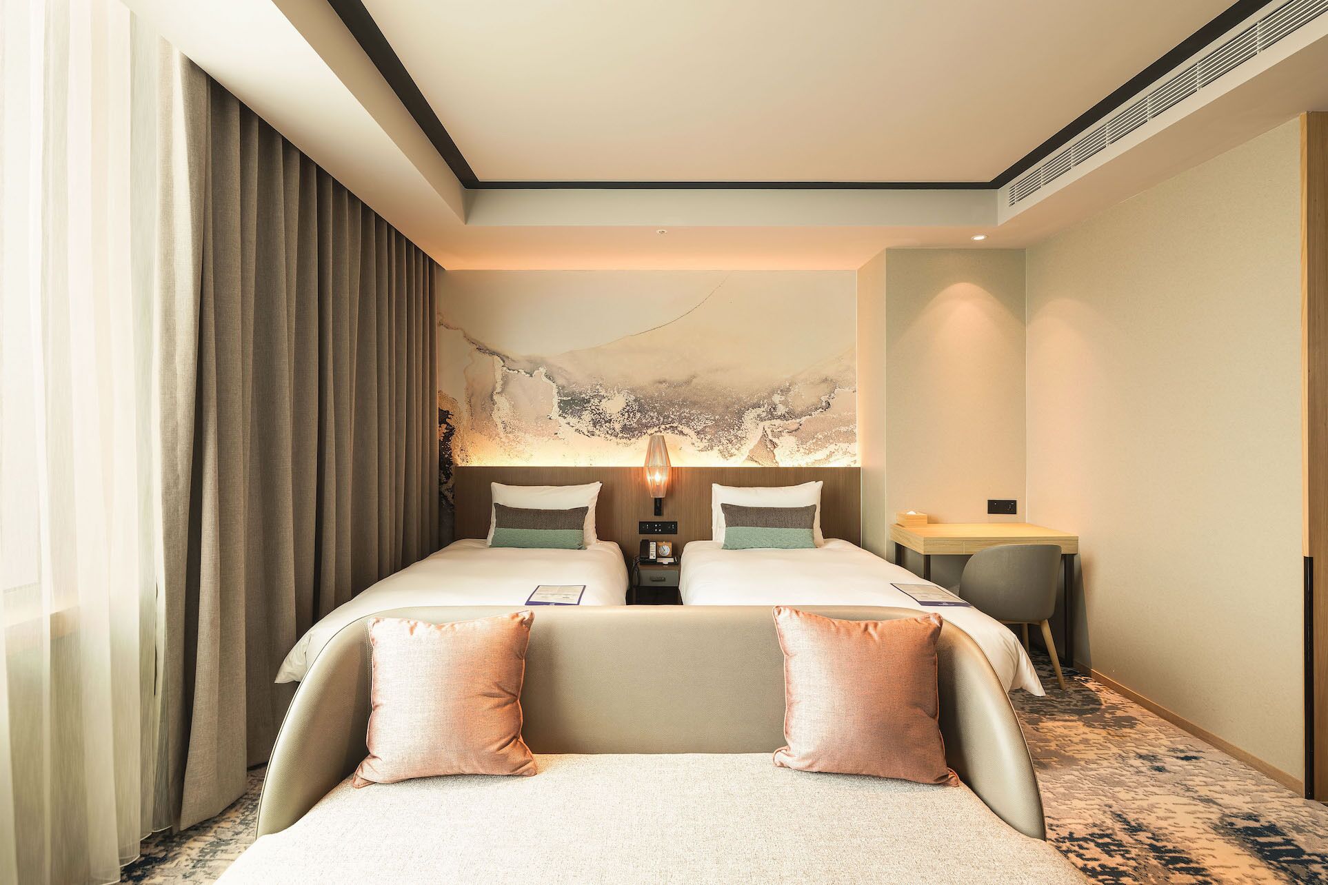 A hotel room with two beds, a desk, a lamp, and a large abstract painting on the wall.