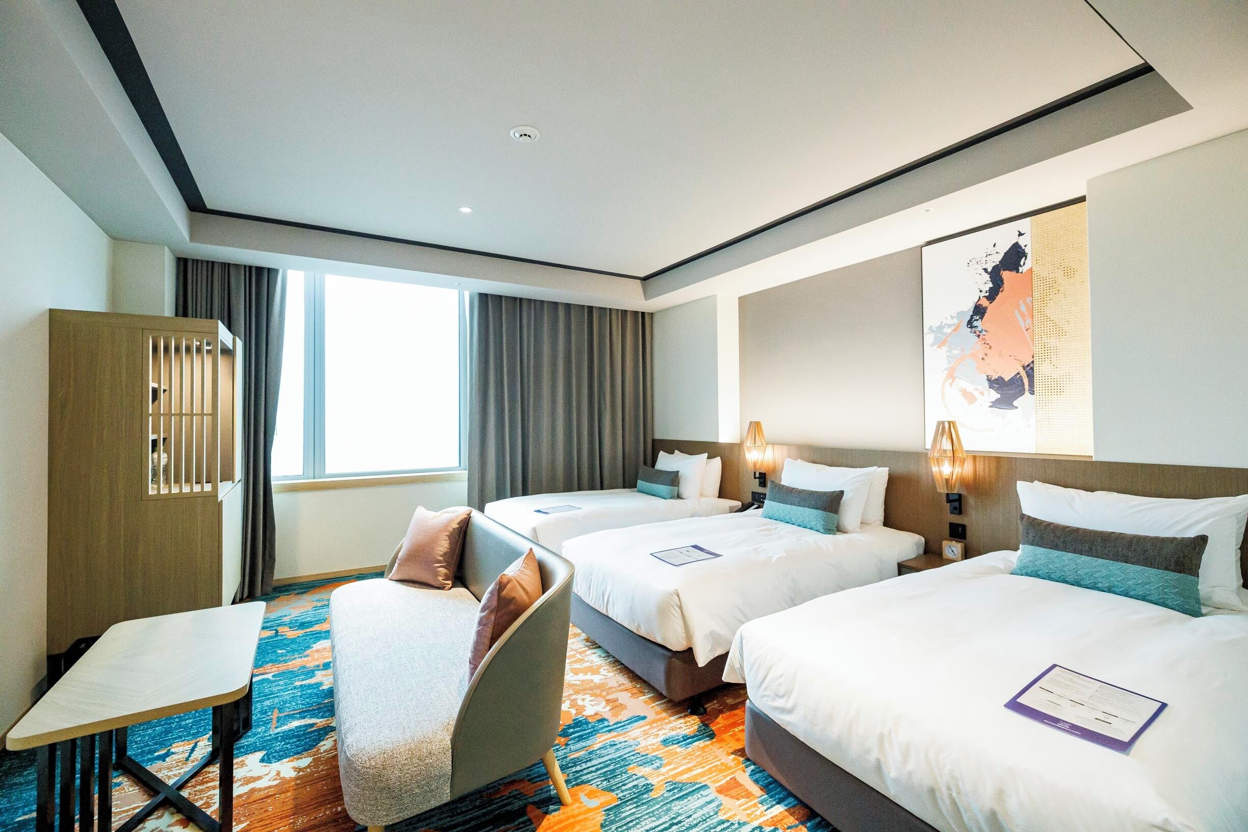 A hotel room with three beds, a desk, and a chair.