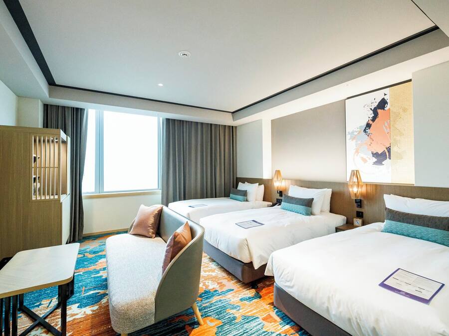 A hotel room with three beds, a desk, and a chair.