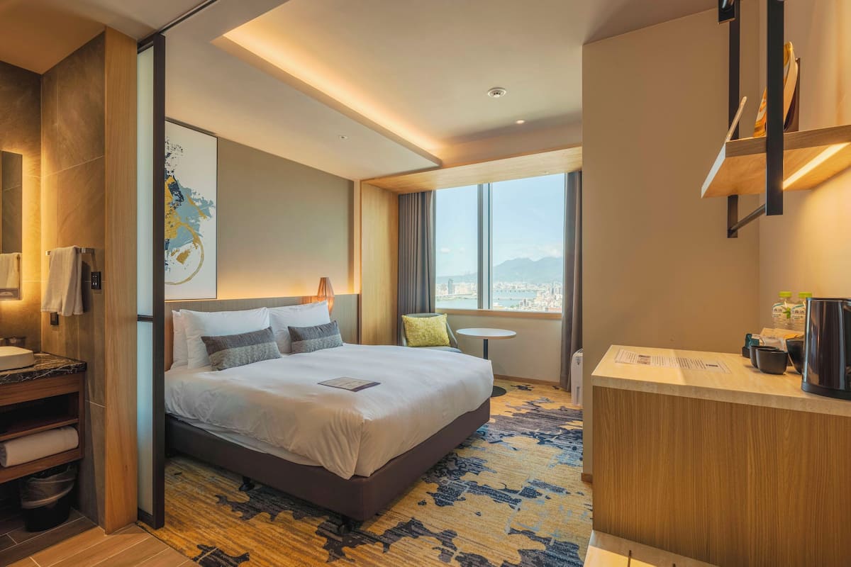 Une chambre d’hôtel moderne dotée d’un grand lit, d’un petit bureau, d’une vue sur la ville et d’une salle de bain avec un lavabo en marbre.