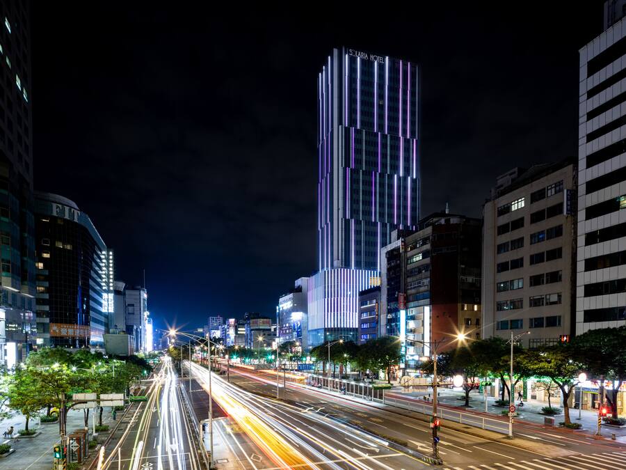 A cityscape at night with illuminated buildings, including a tall hotel with vertical lights.